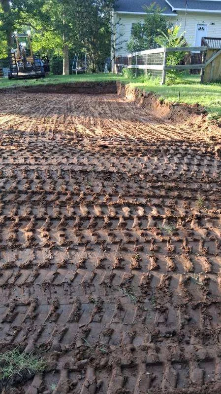 Excavated above-ground pool area in Stoneville, NC, with track marks and a cut edge beside the yard